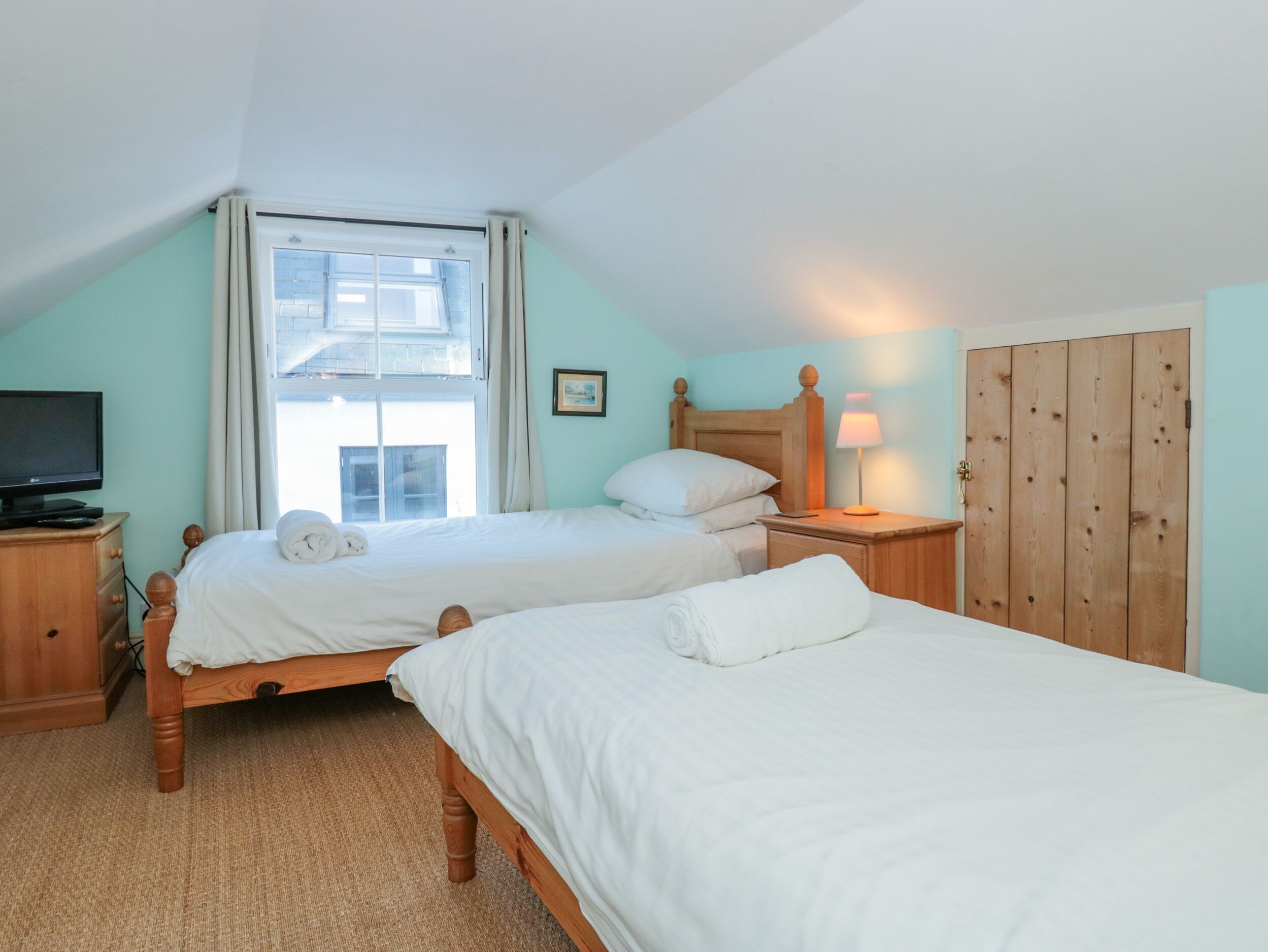 A bedroom with two beds, a television, a lamp, and a wardrobe.