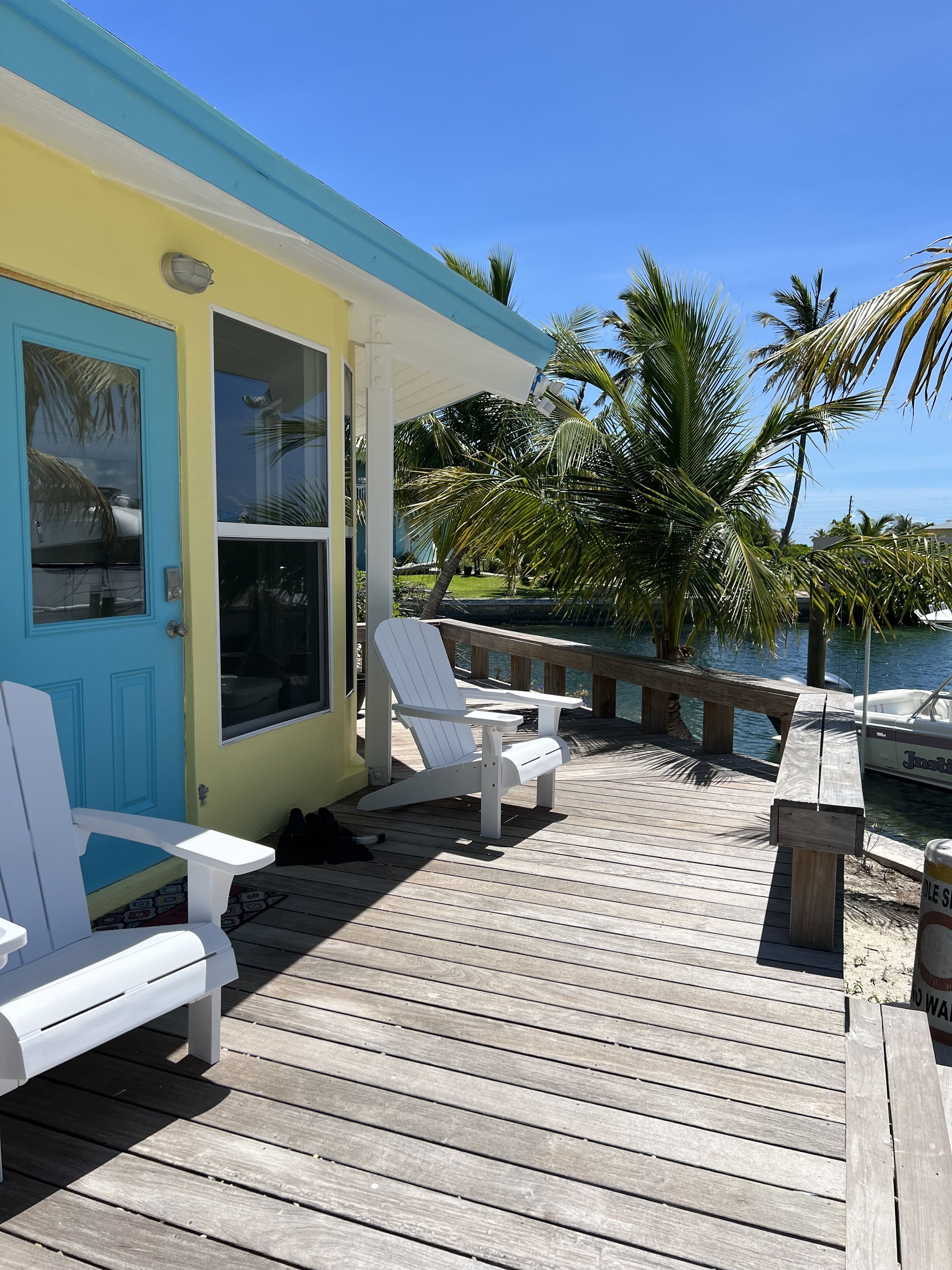 A wooden deck with white Adirondack chairs, a small table, and a bench.