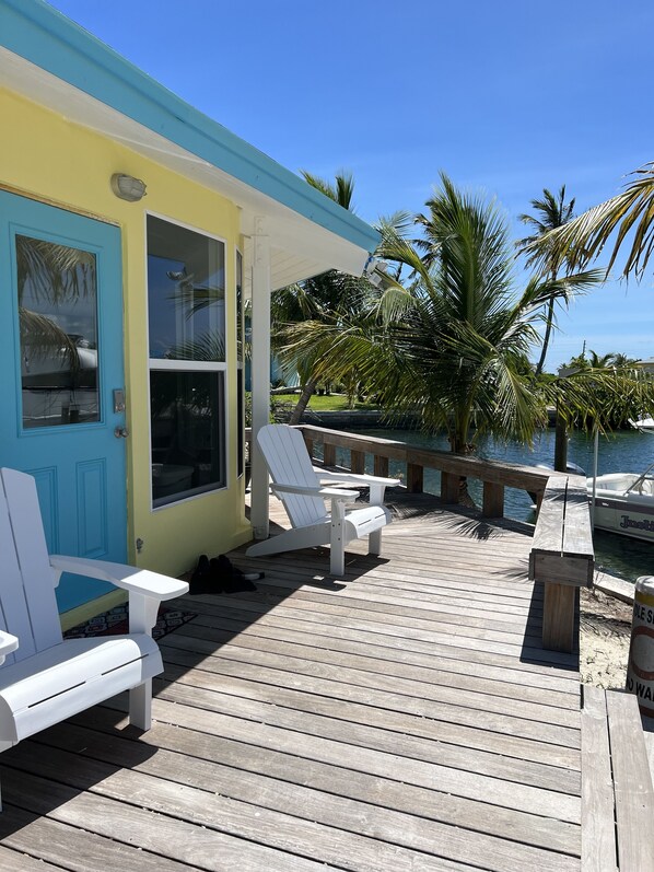 A wooden deck with white Adirondack chairs, a small table, and a bench.