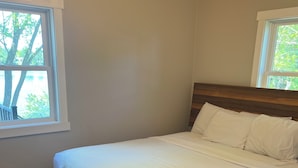 A bedroom with a bed, wooden headboard, and a window with a view of trees.
