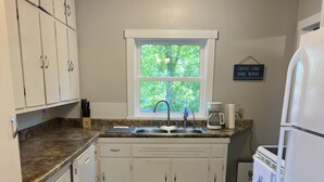 A kitchen with white cabinets, a granite countertop, a window with a view, and a refrigerator.