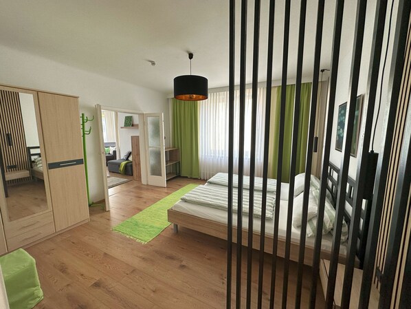 A modern bedroom with a bed, a wardrobe, a seating area, and a green rug.