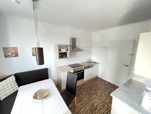 Une cuisine compacte équipée d’un four à micro-ondes, d’une cuisinière et d’un évier. Un coin repas avec une table et des chaises est également disponible.