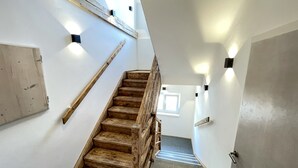 Una escalera de madera con barandilla, paredes blancas y un ventanal en la parte superior.