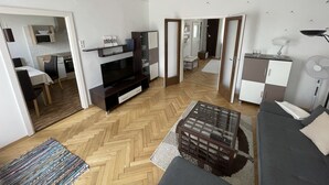Una sala de estar moderna con una televisión de pantalla plana, un sofá, una mesa de centro y un comedor con mesa y sillas.