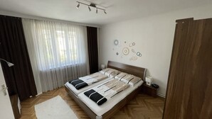 Un dormitorio con cama, mesita de noche, cortinas en la ventana, luz en el techo y adornos circulares en la pared.
