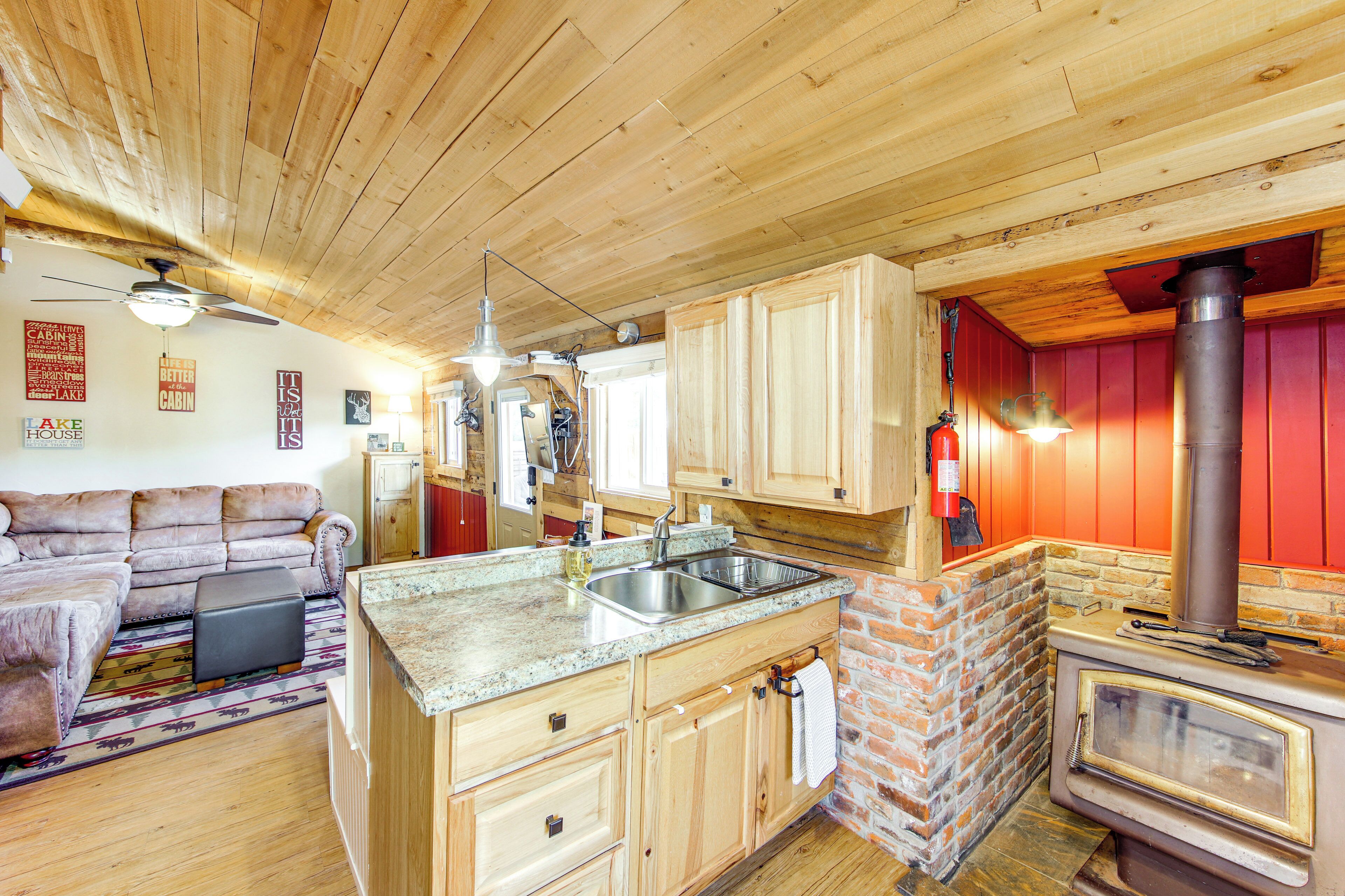 A cabin interior with a kitchen, wooden ceiling, and a fireplace.