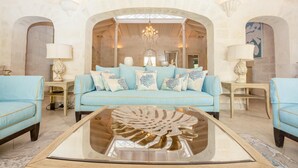 A spacious living room with a light blue sofa, matching armchairs, and a central glass coffee table.
