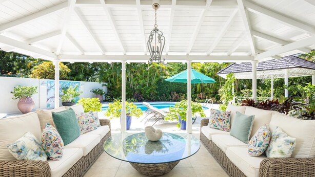 An outdoor patio with wicker sofas, a glass coffee table, and a hanging light fixture.