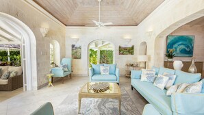 A spacious living room with a high ceiling, two light blue sofas, a coffee table, and a view of greenery through large windows.