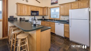 A modern kitchen with wooden cabinets, a central island with stools, a refrigerator, and a window providing natural light. - Cozy Big Horn Home Walking Distance to Big Sky Resort | Ski-In/Out | Fireplace (Big Sky)