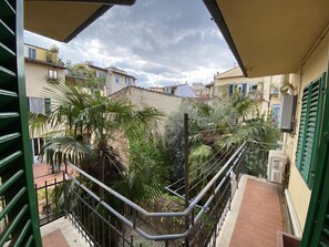 Un balcón con vistas a un patio, que incluye una barandilla de metal, plantas en macetas y un suelo de baldosas.