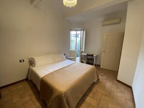 Een slaapkamer met een bed, een bureau en een stoel. Er is een deur en een raam.