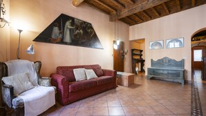 A living room with a red sofa, a white armchair, and a blue bench. There is a painting on the wall and a lamp on a table. - Ruote Apartment first (Firenze)