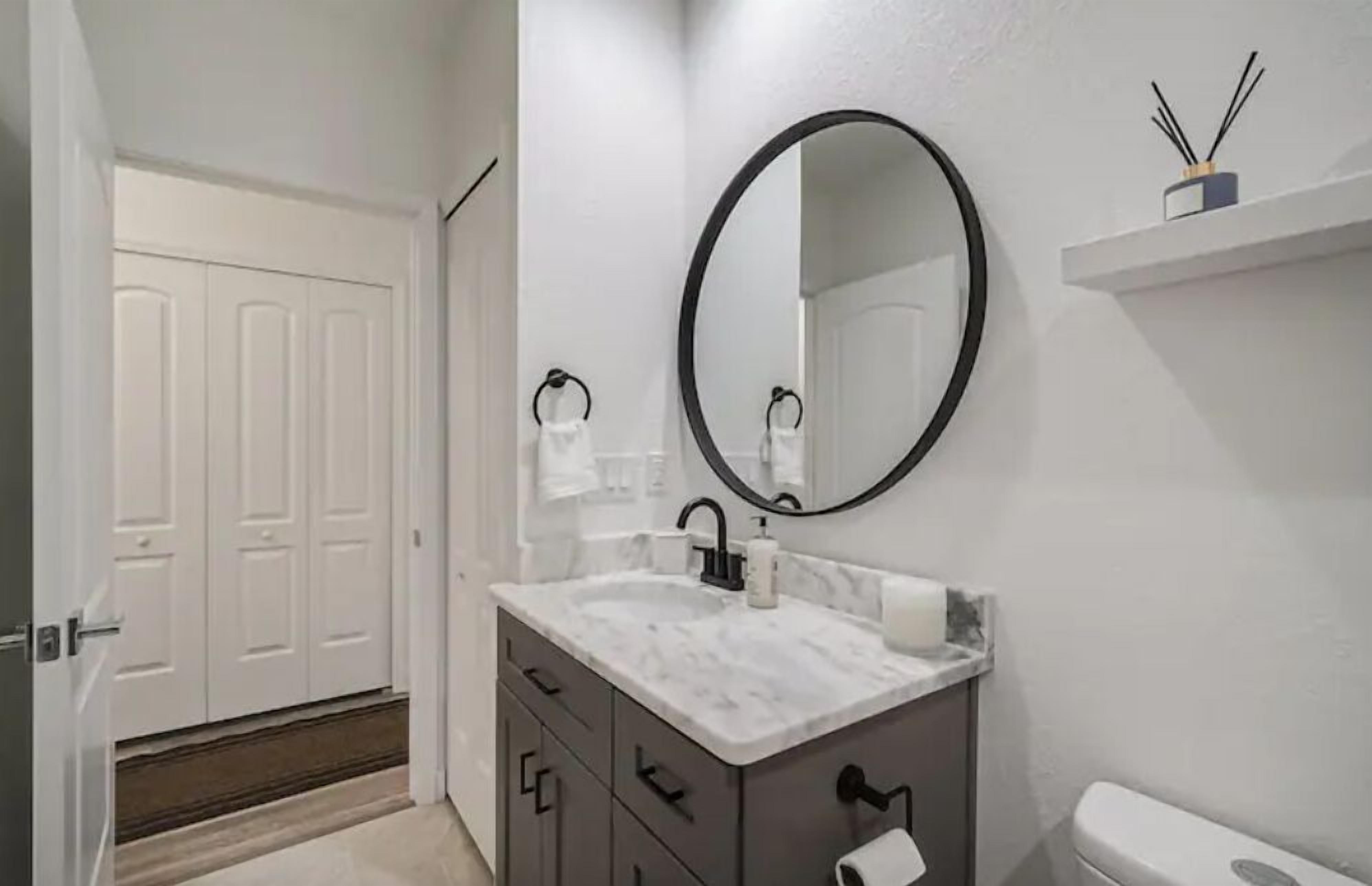 A bathroom with a white vanity, a round mirror, a toilet, and a white door.