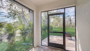 A room with large sliding glass doors leading to a patio with a grassy area and a bench.