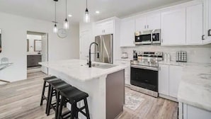 A modern kitchen with white cabinets, stainless steel appliances, and a central island with stools.