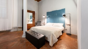 Un dormitorio con cama, un banco, una silla, un escritorio y una lámpara.