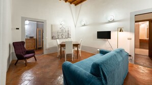 Una habitación con techo de madera, una mesa de comedor con sillas, un sillón morado, un sofá azul y un televisor de pantalla plana.