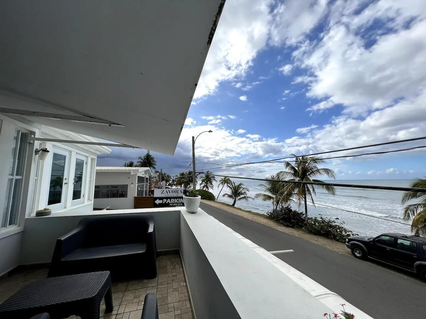 Uma varanda com vista para o oceano, um letreiro com 'Zavora Park & Room' e um carro estacionado.