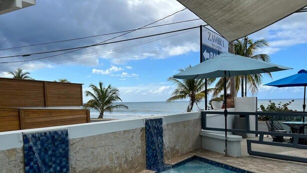 A pool area with a view of the ocean, a bar and room sign, and outdoor seating with umbrellas. - Mares Guesthouse (Aguada)