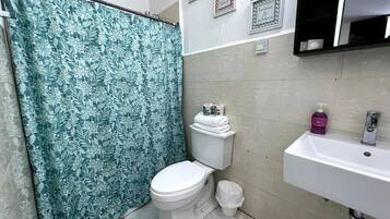 A bathroom with a shower curtain, toilet, sink, and a small trash bin.