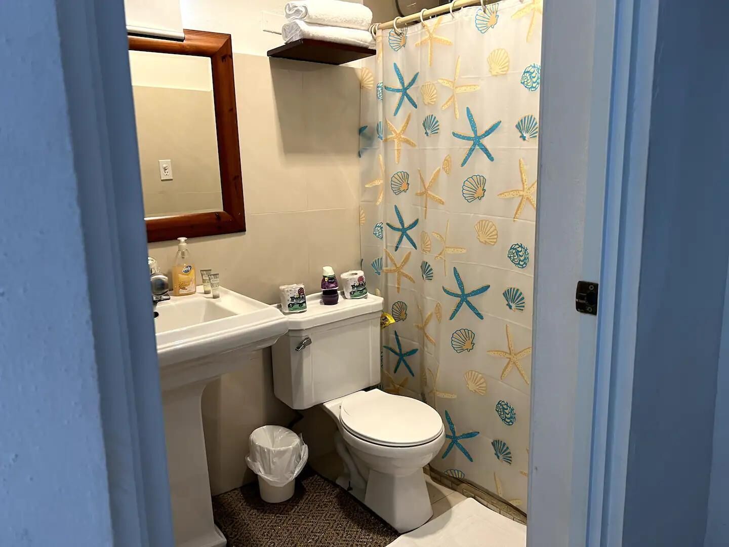 A bathroom with a toilet, sink, and a shower curtain with a starfish and shell pattern.