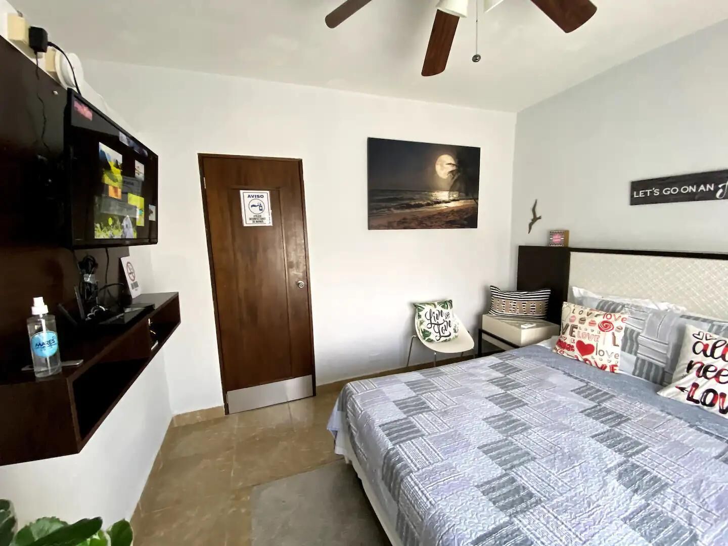 Une chambre à coucher comprenant un lit, un bureau, une chaise, un téléviseur et une porte avec une pancarte.