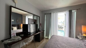 A hotel room with a bed, a desk with a computer, a mirror, and a view of a pool. - Mares Guesthouse (Aguada)