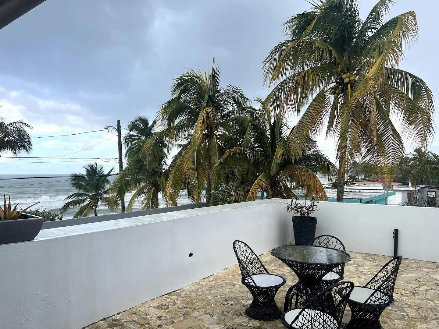 A balcony with a table and chairs, overlooking the sea and palm trees.
