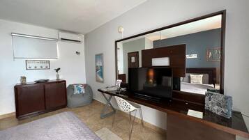 A hotel room with a bed, a desk with a flat-screen TV, a chair, a dresser, and a large mirror.