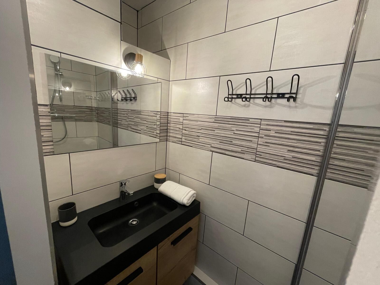 Un baño moderno con un lavabo negro, un espejo, una toalla y una ducha.