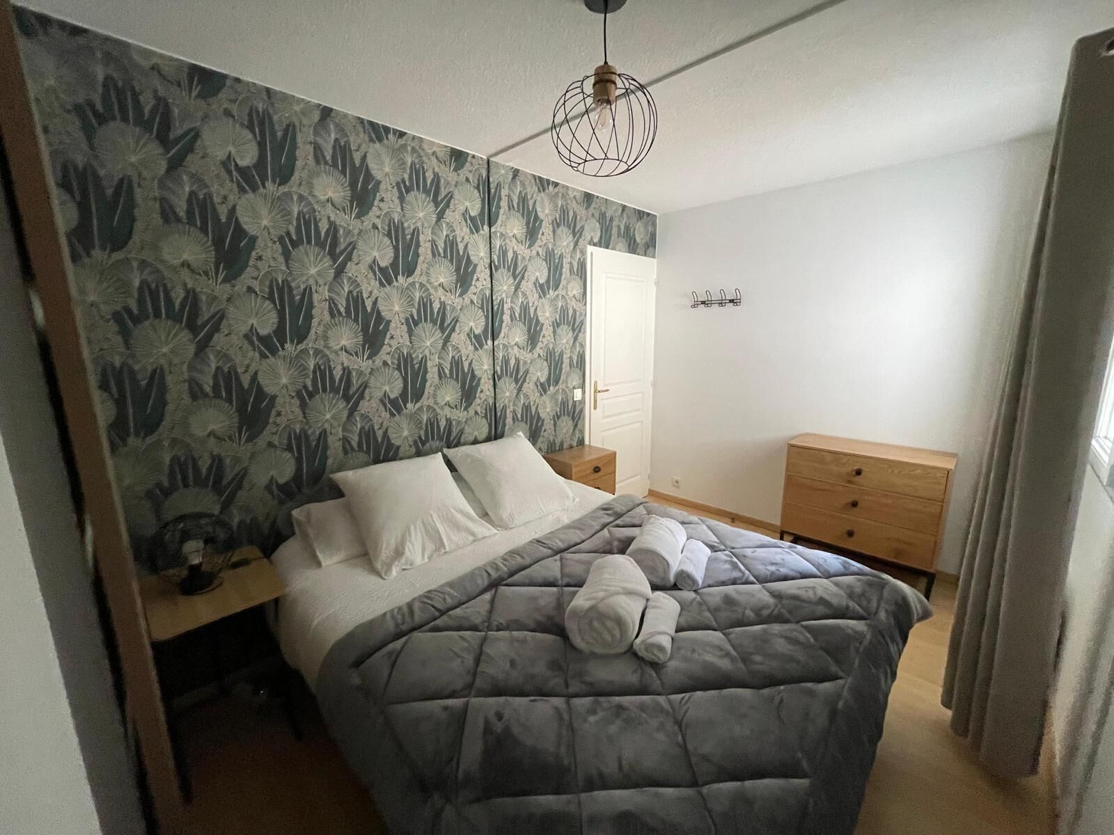 Una camera da letto con un letto, un comodino, una cassettiera e una parete decorata con un motivo floreale.