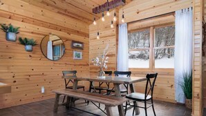 Un interior de madera con una mesa de comedor, sillas, un banco, un espejo y una ventana con cortinas.