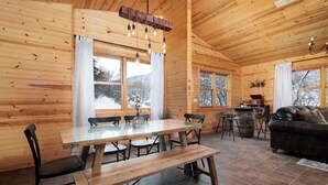 Interior de una cabaña de madera con una mesa de comedor, sillas, un sofá y una chimenea.