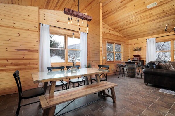 Interior de una cabaña de madera con una mesa de comedor, sillas, un sofá y una chimenea.