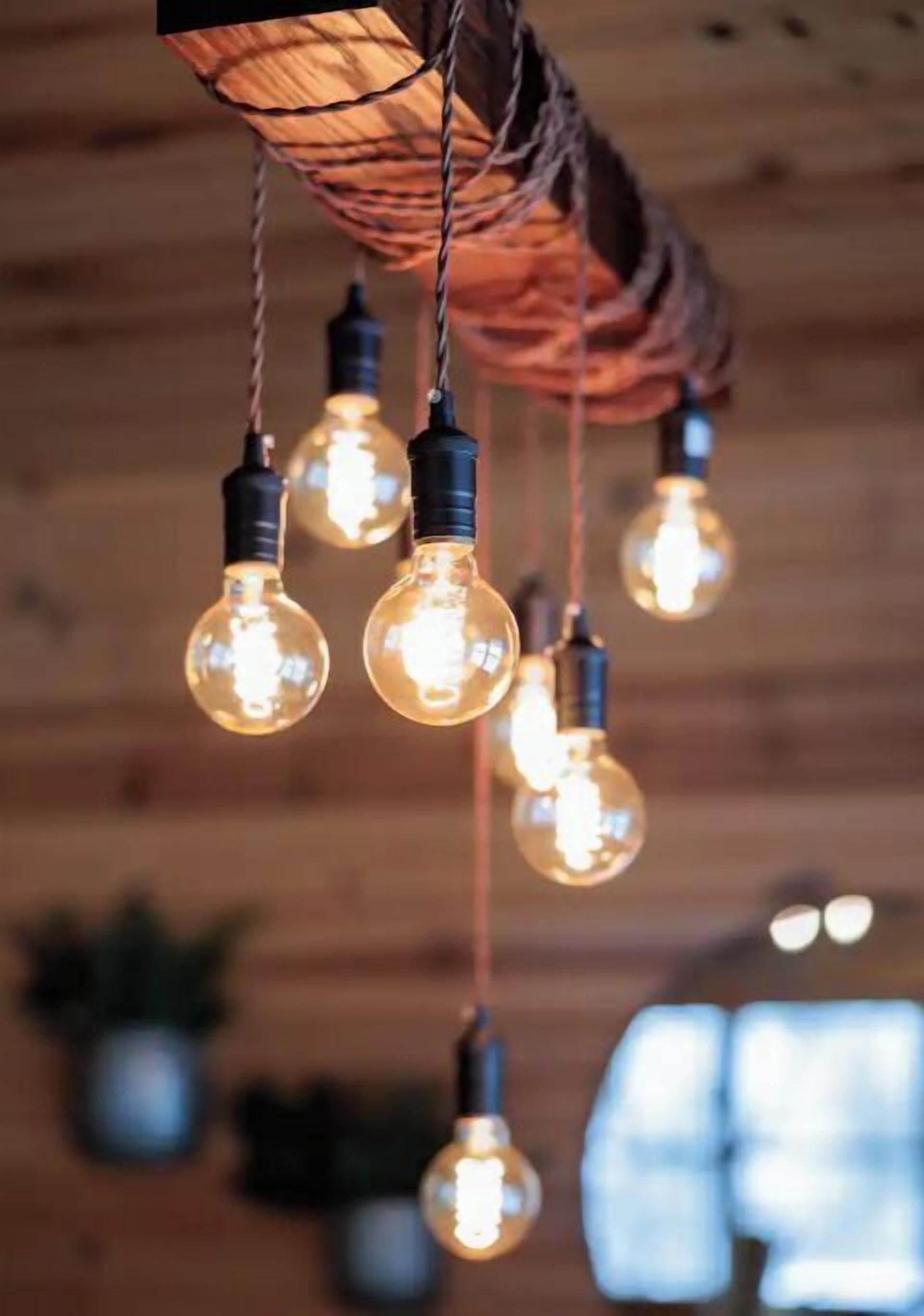 Une série de suspensions lumineuses composées d’ampoules apparentes, suspendues à un plafond en bois.