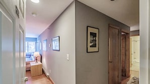 A hallway with a wooden floor, a door on the left, and a framed picture on the wall.
