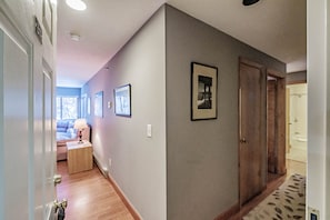 Ein Korridor mit Holzboden, einer Tür links und einem gerahmten Bild an der Wand.