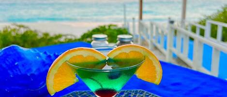 Ein Cocktail auf einem blauen Tisch mit Blick auf den Sonnenuntergang über dem Meer.