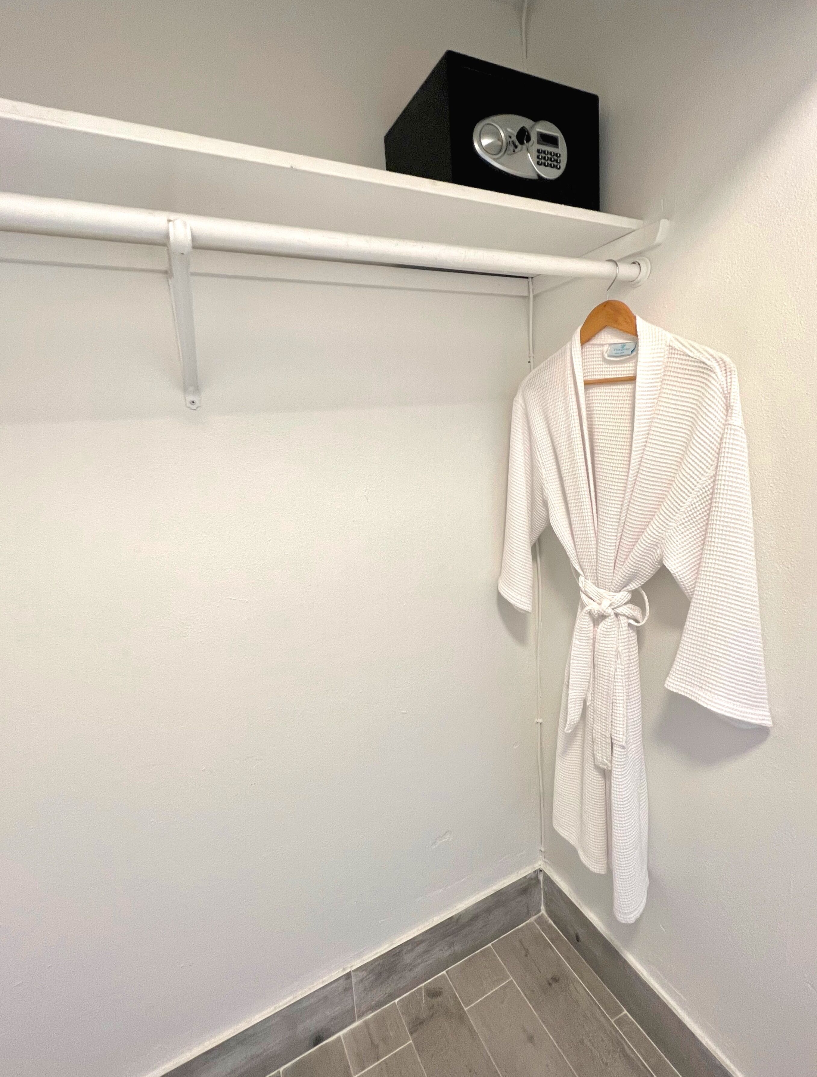 A white robe hanging on a wooden hanger in a bathroom with a white wall and a tiled floor.