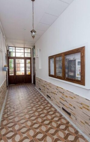 Un couloir au sol carrelé, une porte en bois au fond et un tableau encadré accroché au mur.