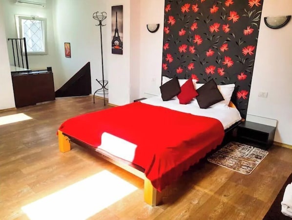 Une chambre à coucher comprenant un lit, une table de chevet, une lampe sur pied, une chaise, un bureau et une fenêtre.