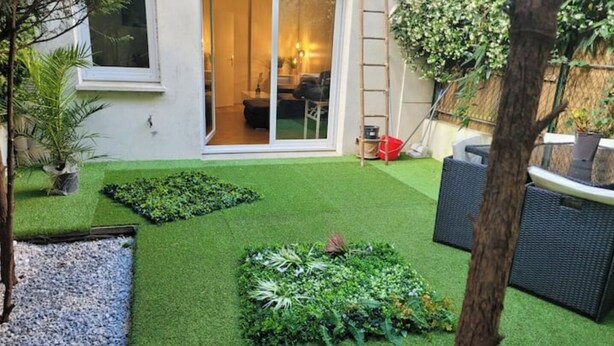 Un jardín bien cuidado con césped artificial, un sendero de grava y mobiliario de exterior.