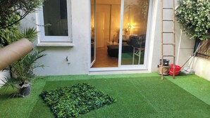 Un patio pequeño con césped artificial, una planta en maceta y una escalera apoyada en la pared.