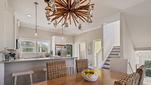 A modern kitchen with white cabinetry, a wooden dining table, wicker chairs, and a unique chandelier.