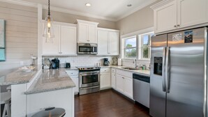 A modern kitchen with white cabinets, stainless steel appliances, a granite countertop, and a hanging light fixture.