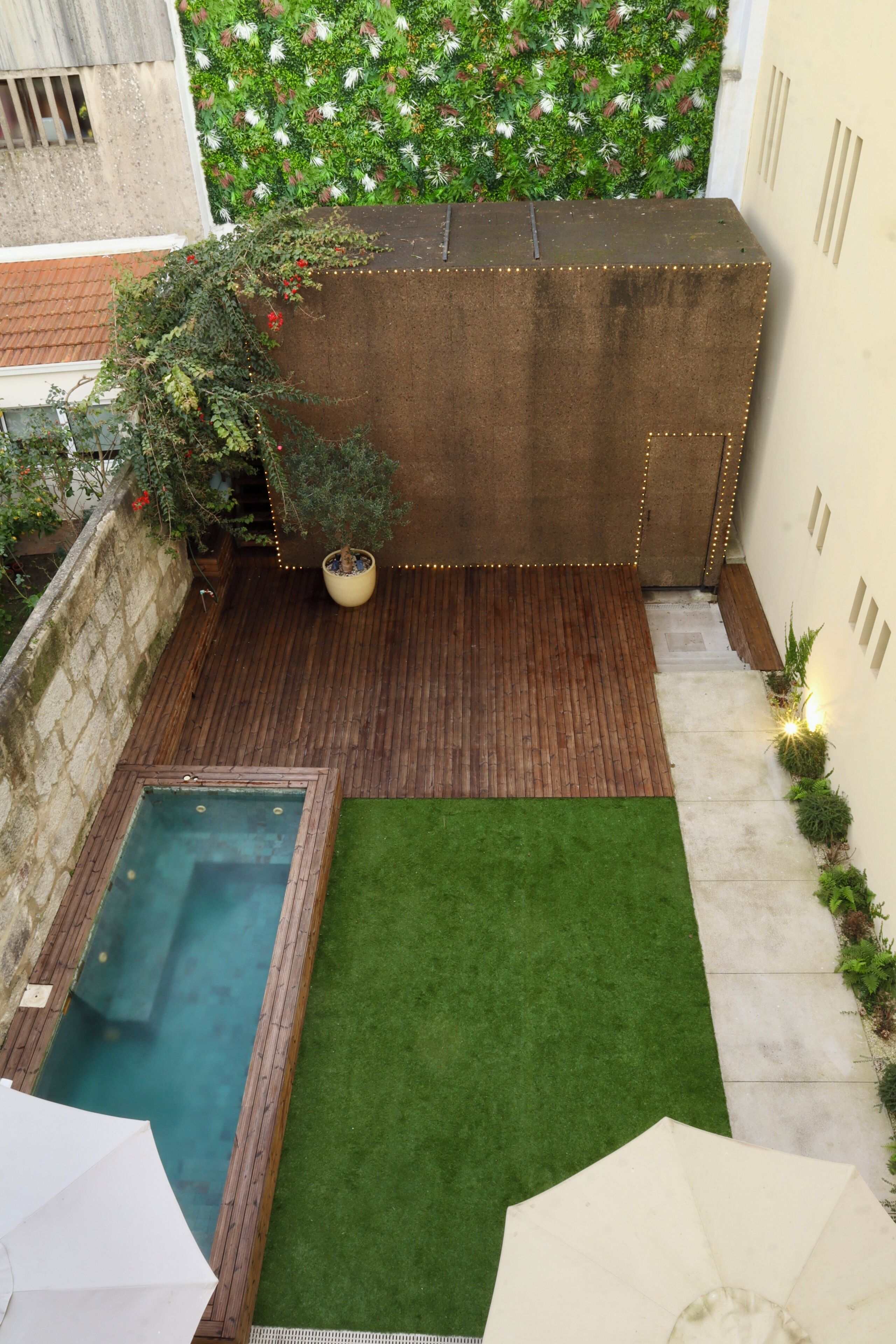 Un pequeño patio con terraza de madera, una piscina pequeña y un césped verde.