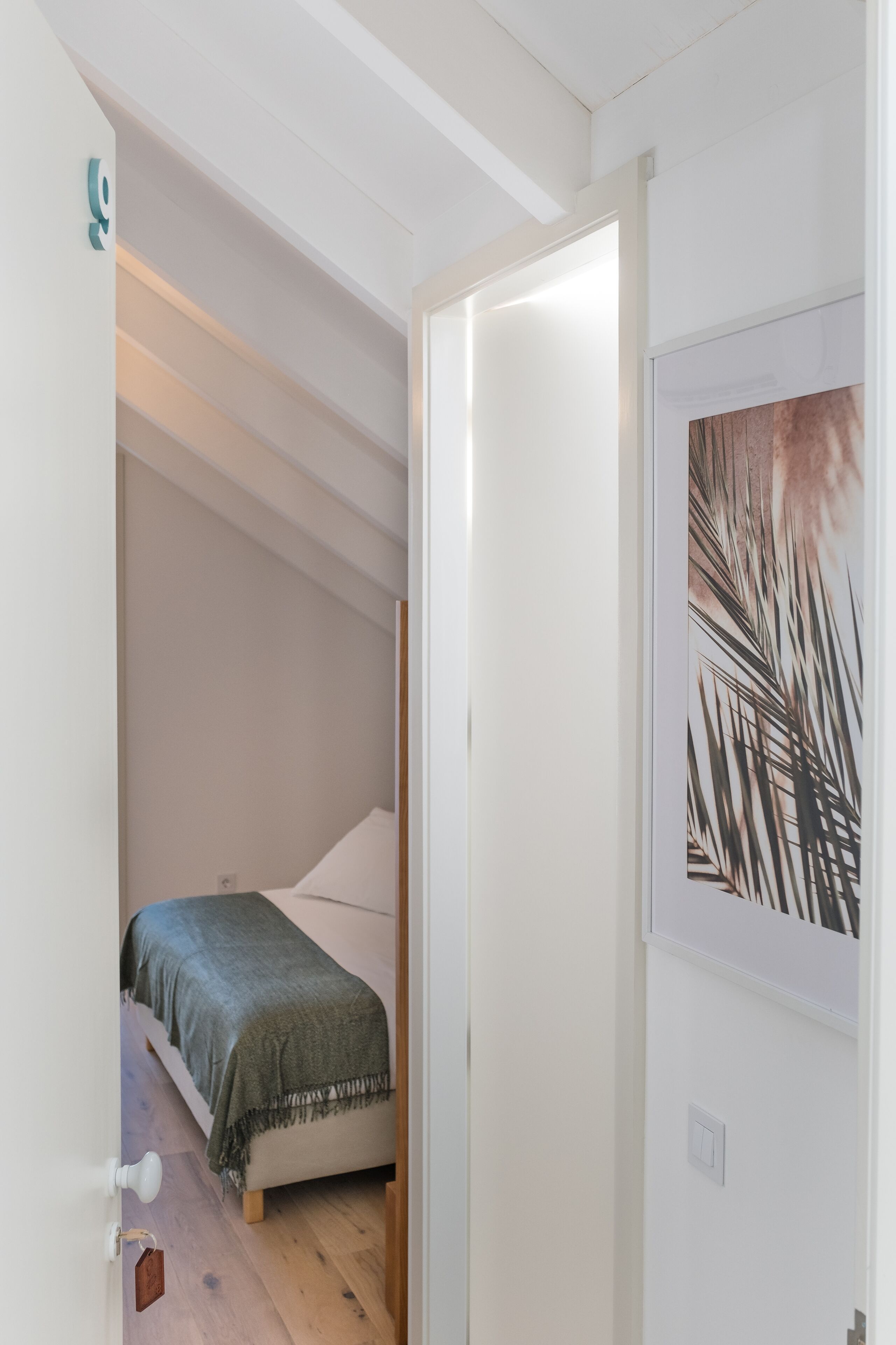 A bedroom with a bed, a door, and a wall with a framed picture.