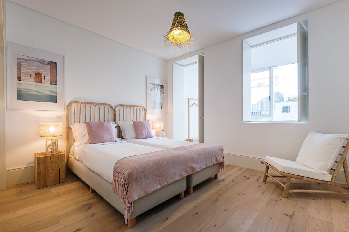 Ein Schlafzimmer mit einem großen Bett, Nachttischlampen, einem Sessel und einem Fenster.